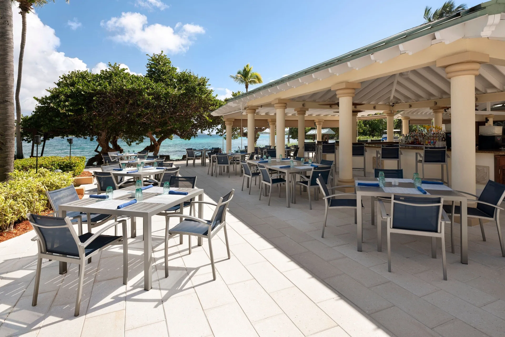 Seaside outdoor restaurant with shaded tables and a bar at The Ritz-Carlton, St. Thomas.