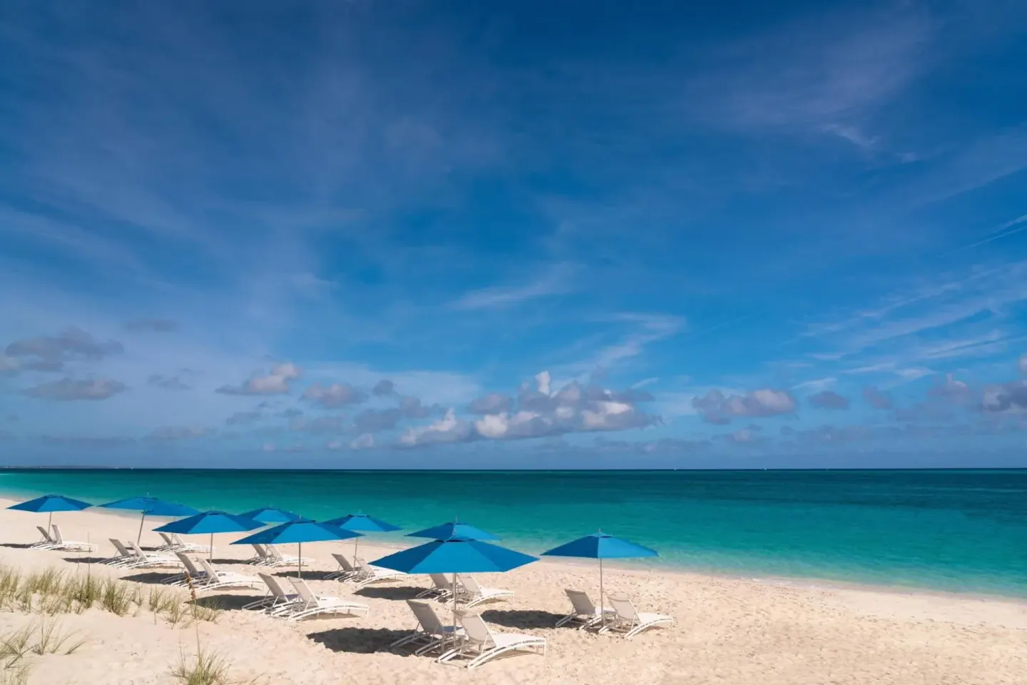 Beach at The Ritz-Carlton, Turks & Caicos with blue umbrellas, lounge chairs, white sand, and calm sea.