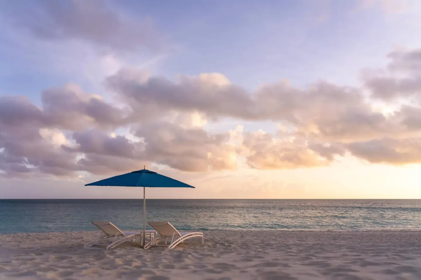 Beach loungers under a blue umbrella at sunset at The Ritz-Carlton, Turks & Caicos.