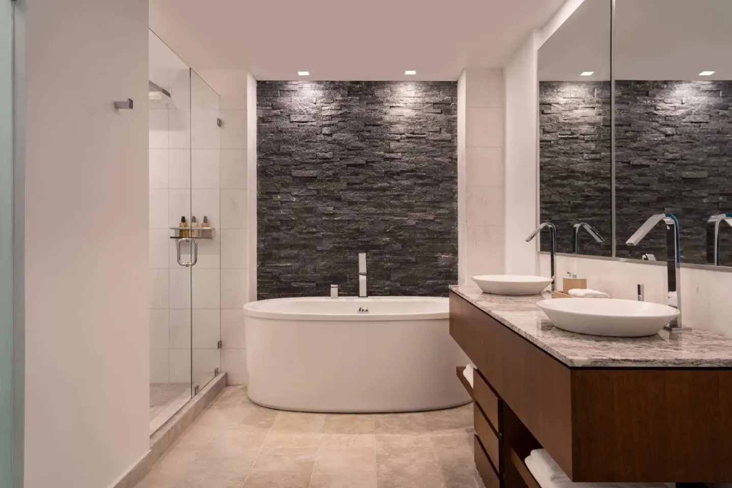 Bathroom at The Ritz-Carlton, Turks & Caicos with soaking tub, glass shower, dual sinks, and stone accent wall.