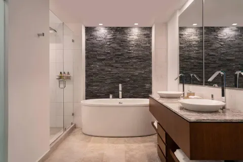 Bathroom at The Ritz-Carlton, Turks & Caicos with soaking tub, glass shower, dual sinks, and stone accent wall.