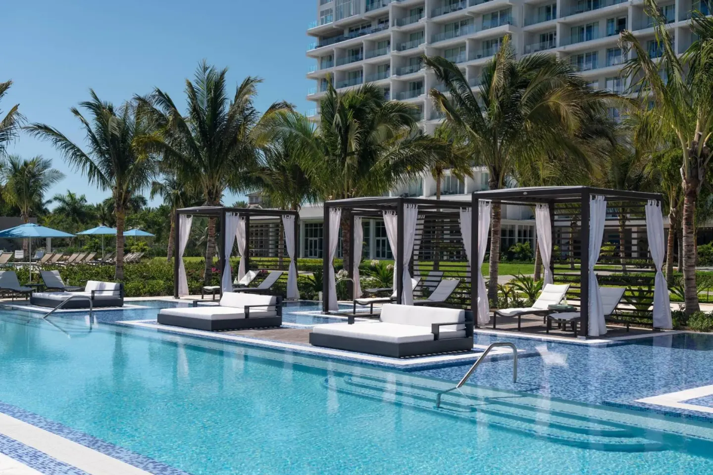 Poolside cabanas and palm trees beside the resort tower at The Ritz-Carlton, Turks & Caicos.