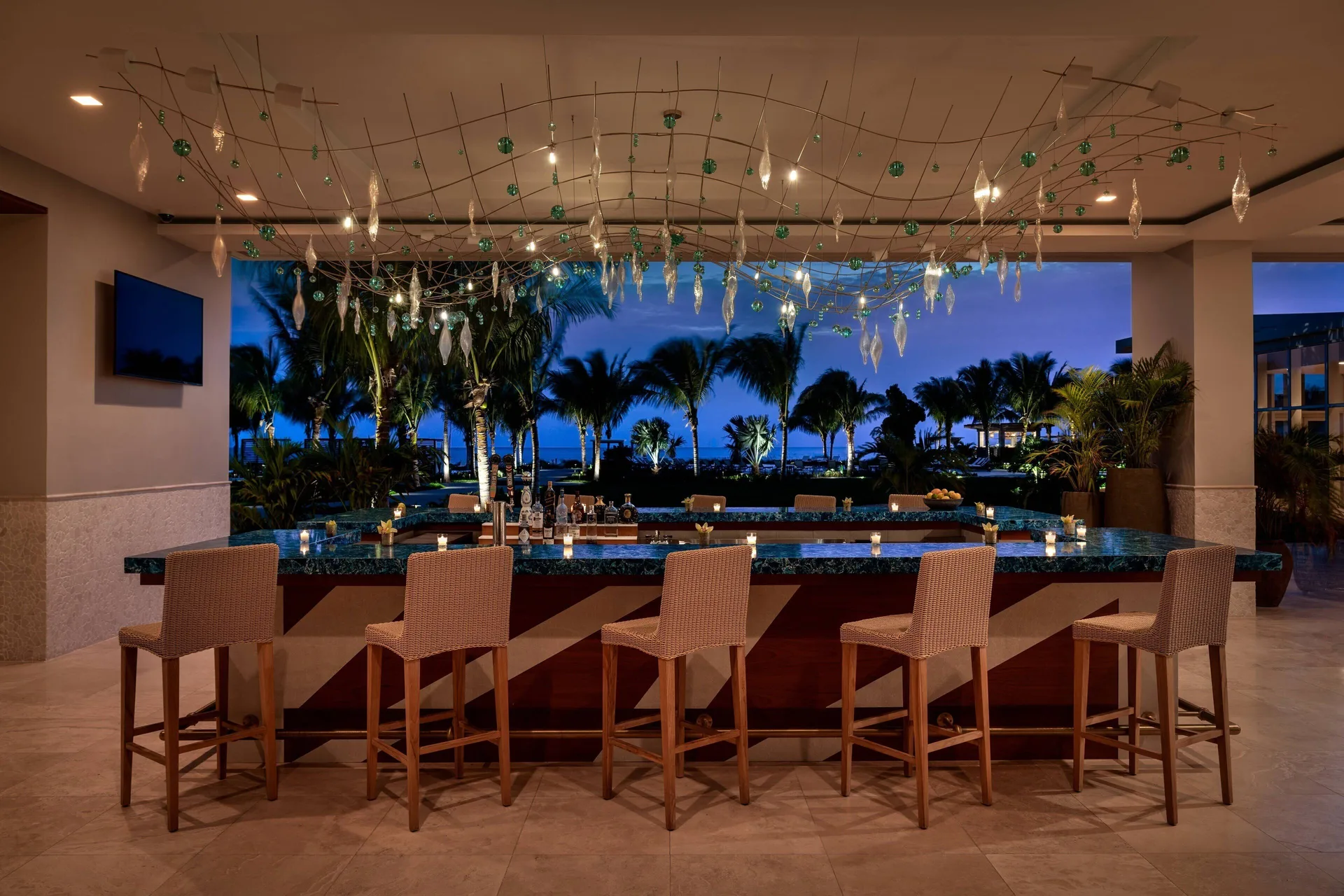 Lobby bar at The Ritz-Carlton, Turks & Caicos with woven stools and a palm-framed ocean view.