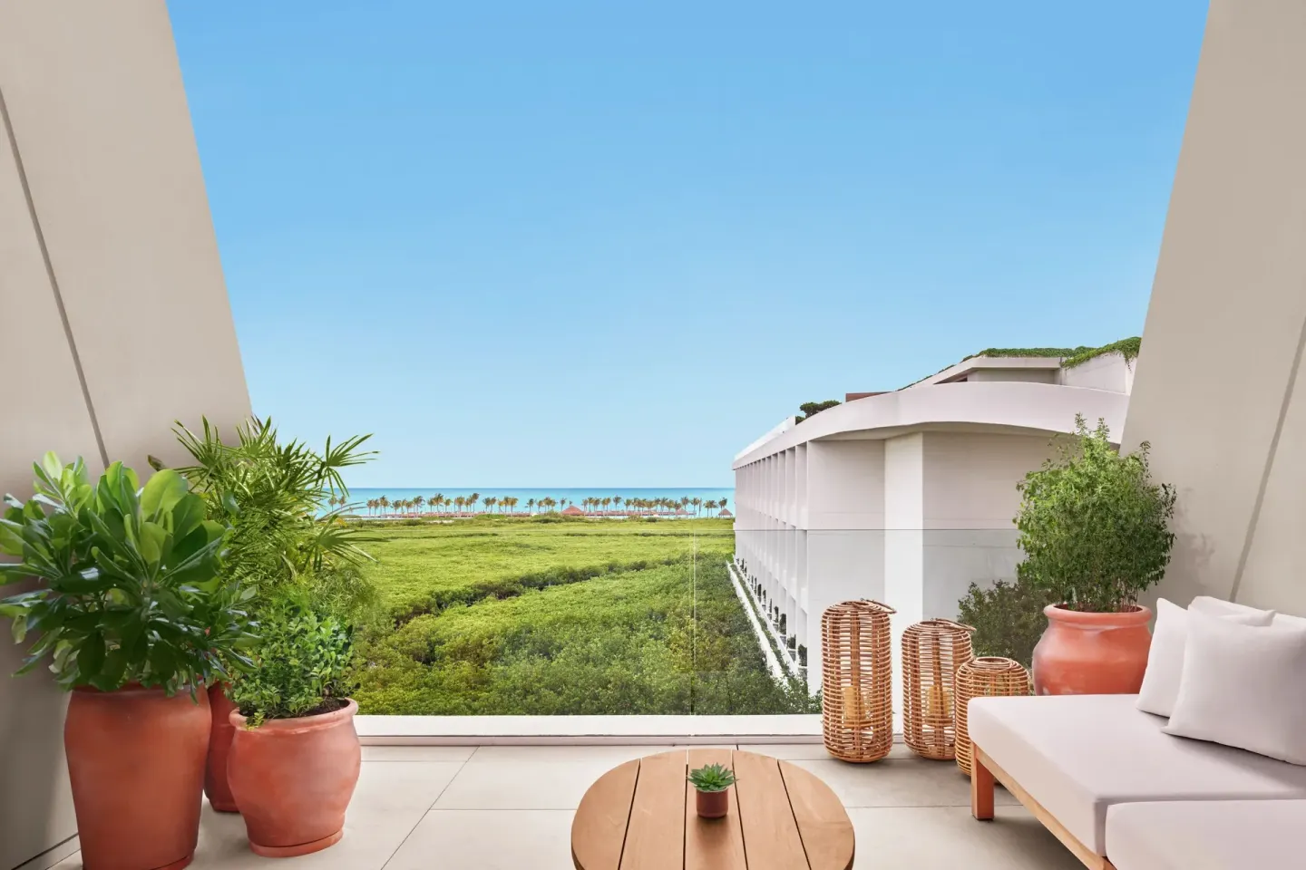 Balcony lounge framed by plants and ocean horizon at The Riviera Maya EDITION At Kanai.