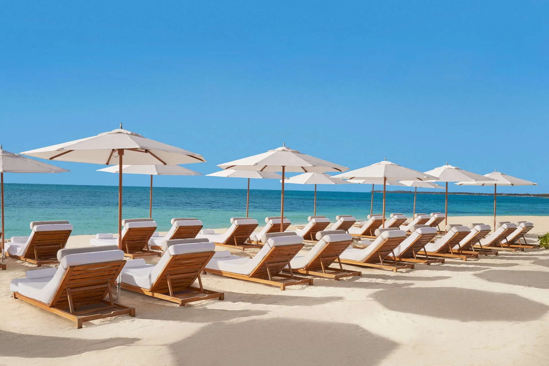 Rows of beach loungers and white umbrellas at The Riviera Maya EDITION At Kanai.