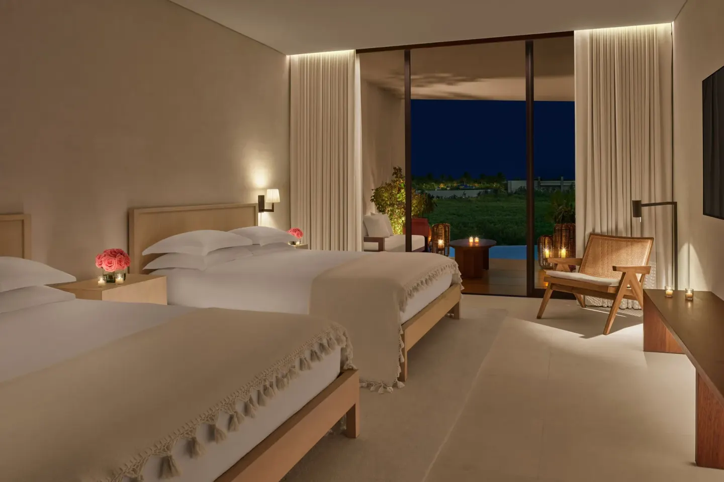 Two-bed guest room at The Riviera Maya EDITION At Kanai with candlelit terrace at night.