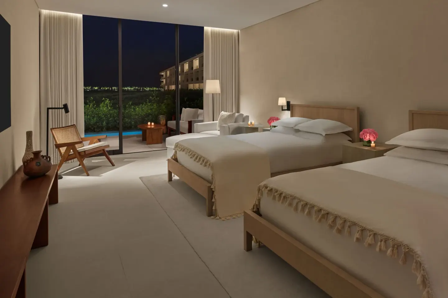 Two-bed guest room at The Riviera Maya EDITION At Kanai opening to a terrace at night.