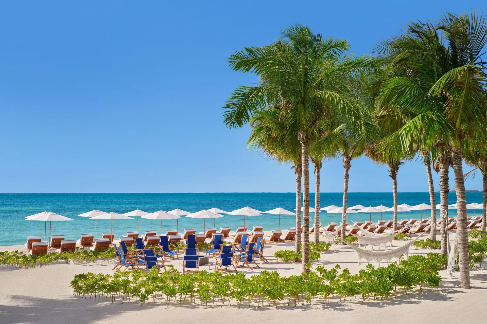 Beach lounge chairs, umbrellas and palms at The Riviera Maya EDITION At Kanai.
