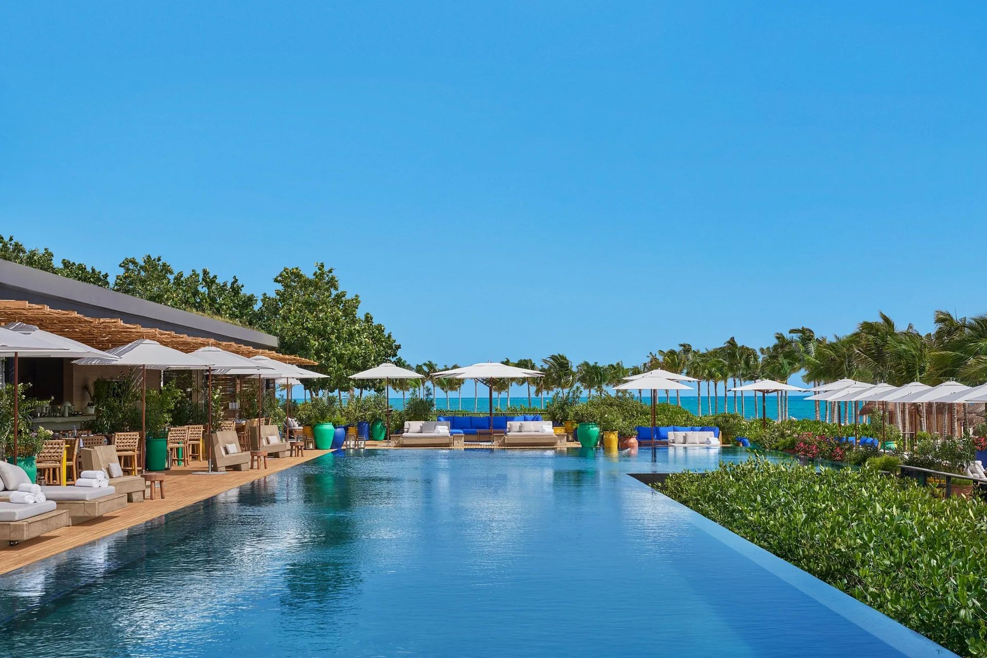 Resort pool with loungers, umbrellas and ocean beyond at The Riviera Maya EDITION At Kanai.