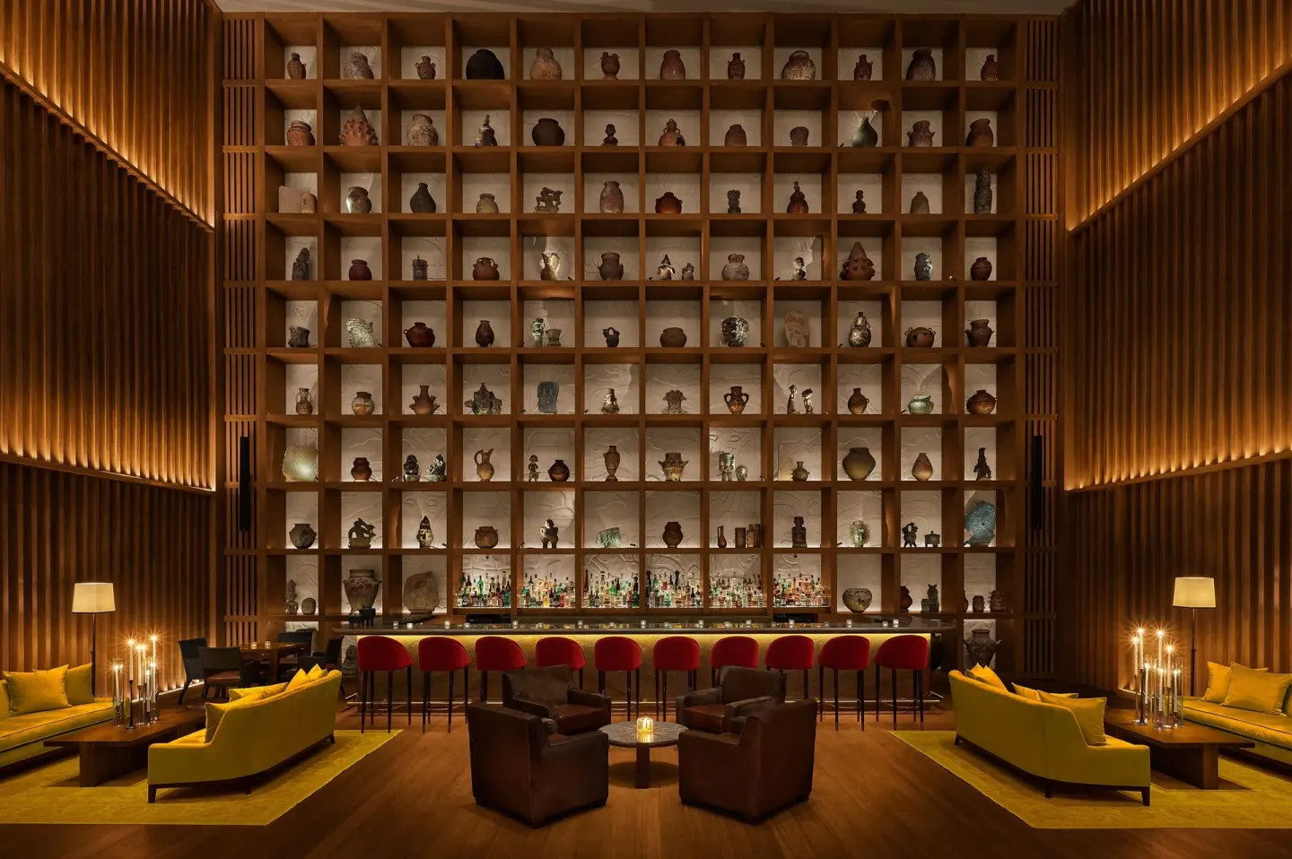 Lobby bar with red stools and a pottery display at The Riviera Maya EDITION At Kanai.
