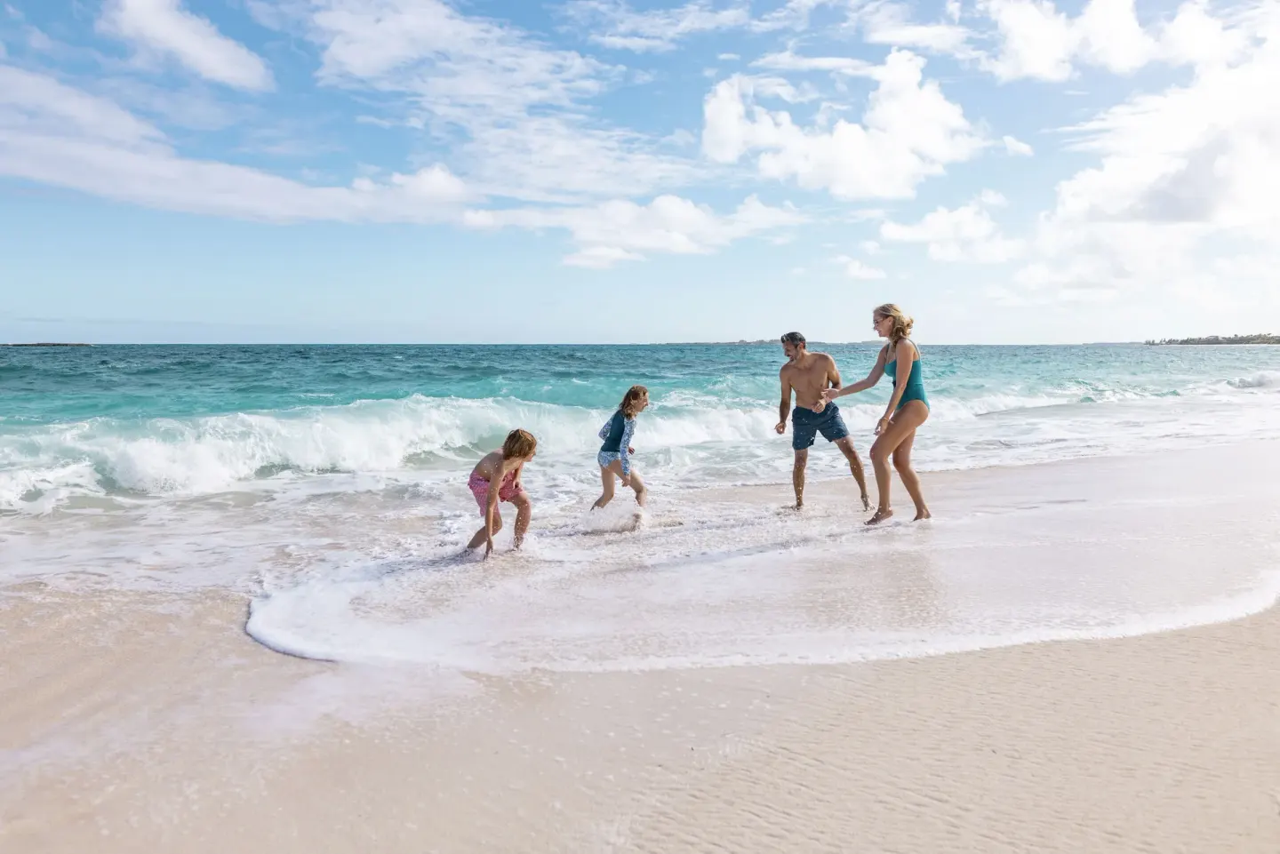 Family playing in the surf on a sandy beach at The Royal at Atlantis.