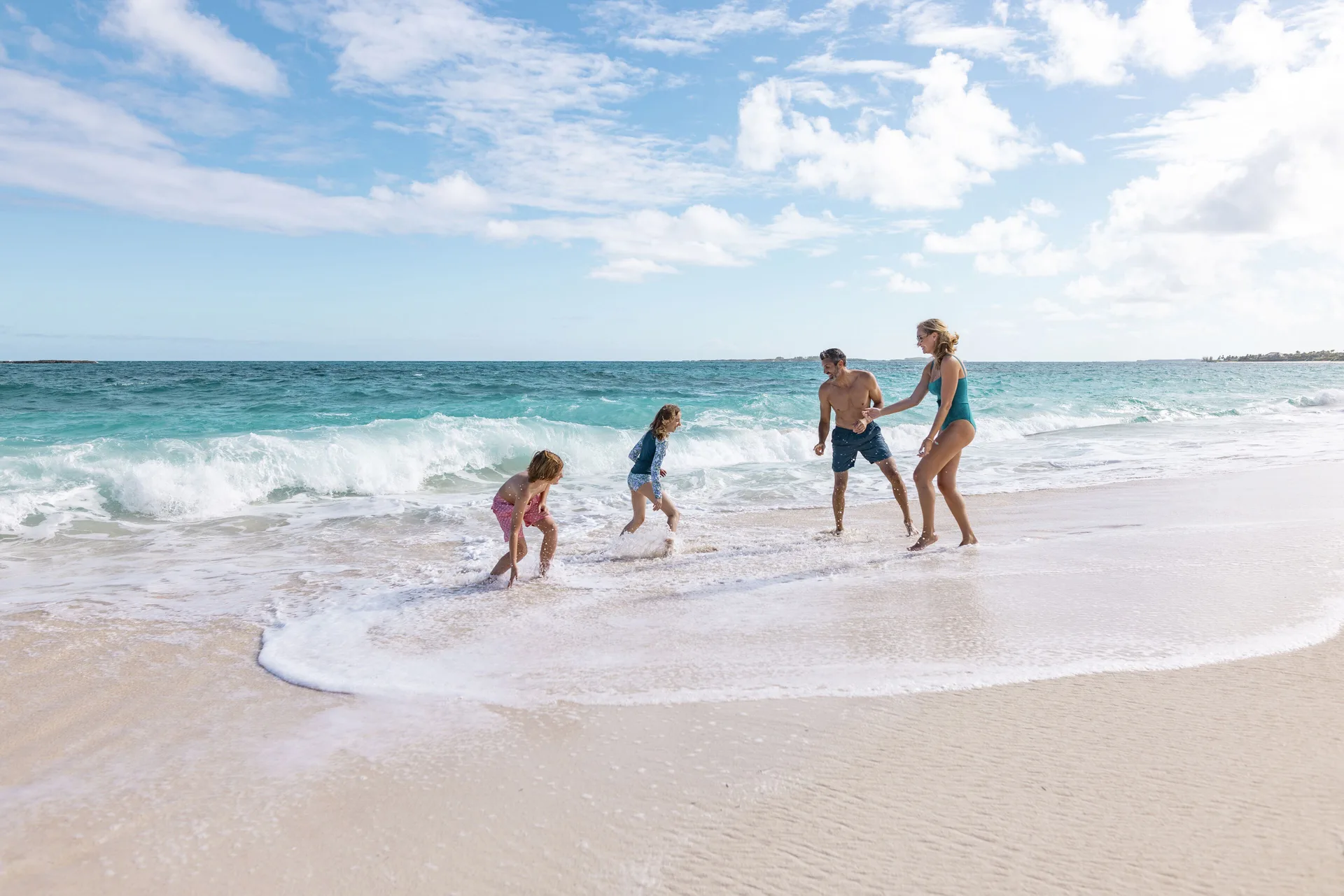 Family playing in the surf on a sandy beach at The Royal at Atlantis.