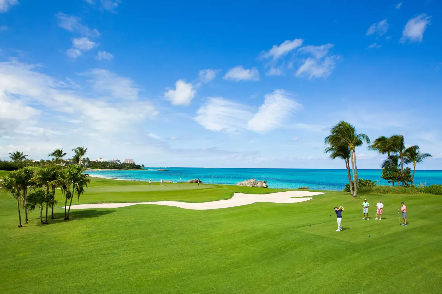 Oceanfront golf green with palm trees and golfers at The Royal at Atlantis.