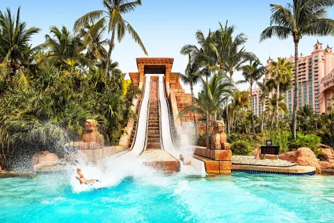 A tall waterslide splashes into a pool amid palms at The Royal at Atlantis.