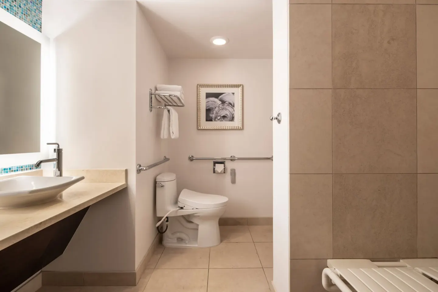Accessible bathroom with vanity, toilet, grab bars and tiled shower at The Royal Hawaiian, Waikiki.