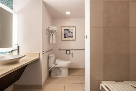 Accessible bathroom with vanity, toilet, grab bars and tiled shower at The Royal Hawaiian, Waikiki.