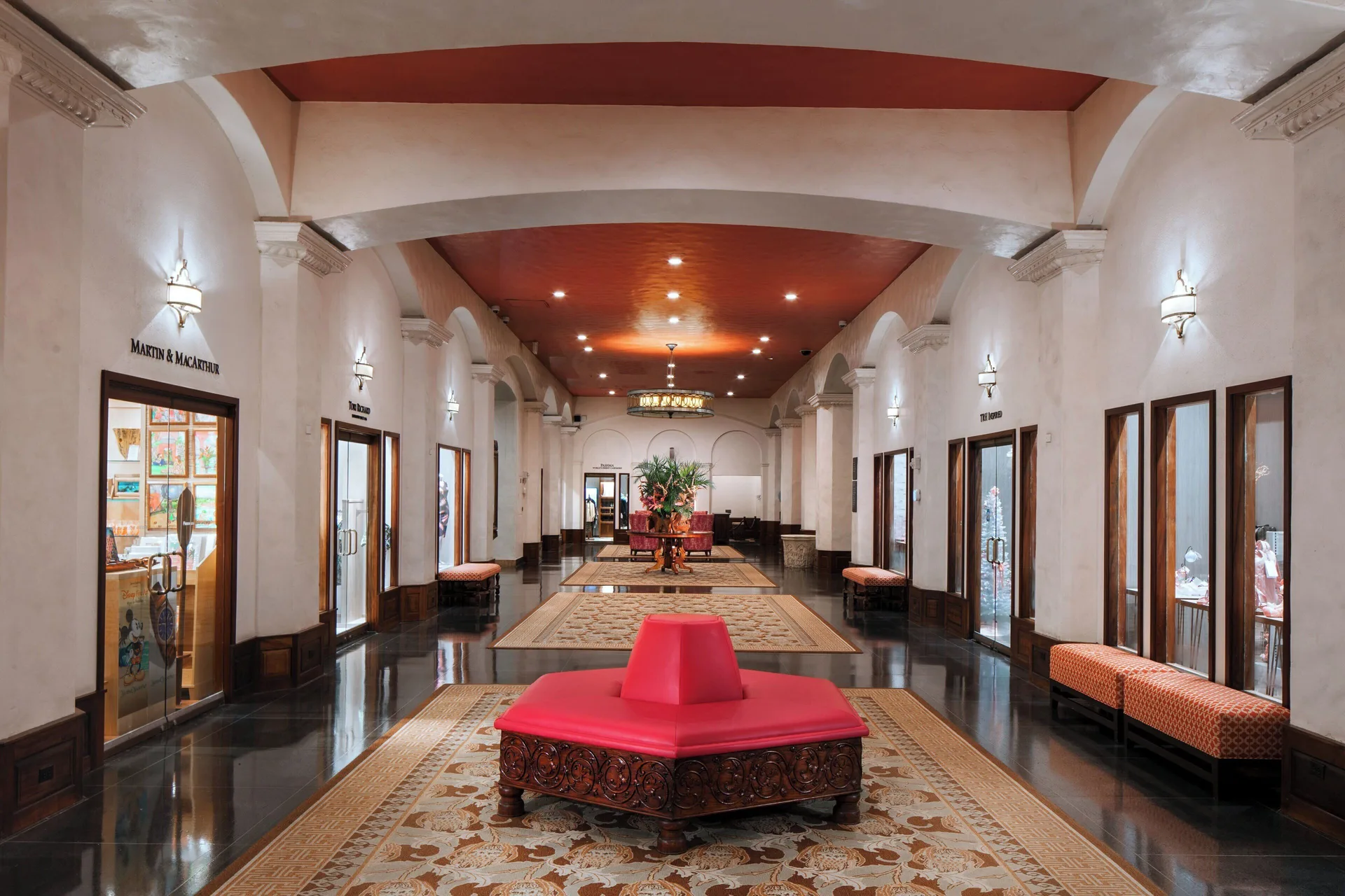 Arched shopping corridor with red bench seating inside The Royal Hawaiian, Waikiki.