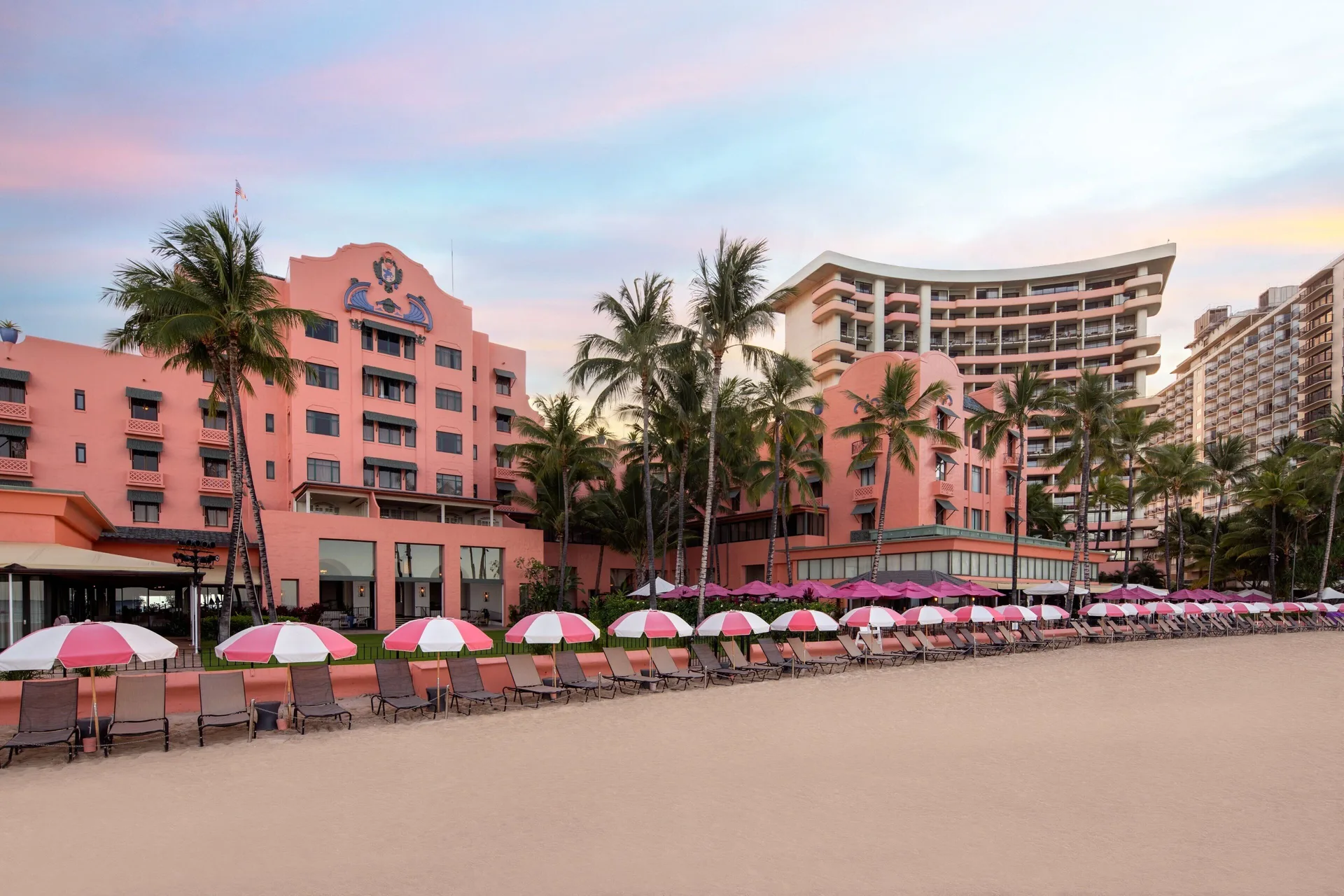 Pink resort buildings and beachfront umbrellas at dusk at The Royal Hawaiian, Waikiki.