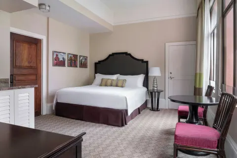 King bed guest room with sitting table and tall windows at The Royal Hawaiian, Waikiki.