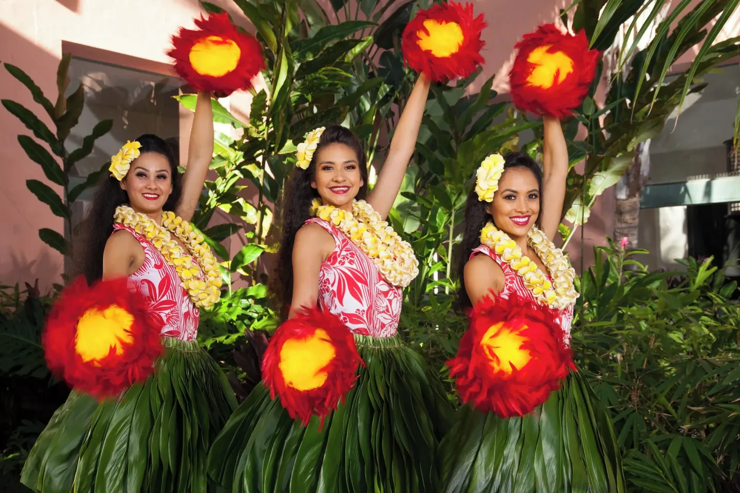 Three hula dancers pose with feathered implements at The Royal Hawaiian, Waikiki.