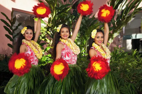 Three hula dancers pose with feathered implements at The Royal Hawaiian, Waikiki.
