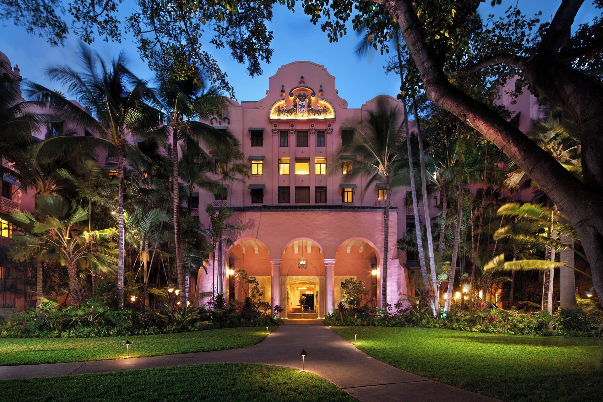 Illuminated pink resort entrance and palms at The Royal Hawaiian, Waikiki at dusk.
