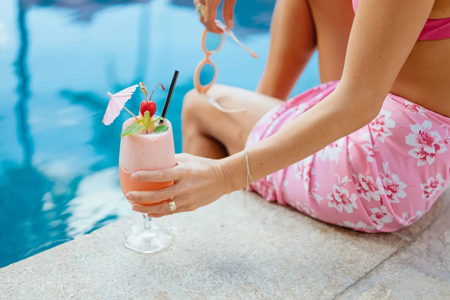 Pink poolside cocktail held beside blue water at The Royal Hawaiian, Waikiki.