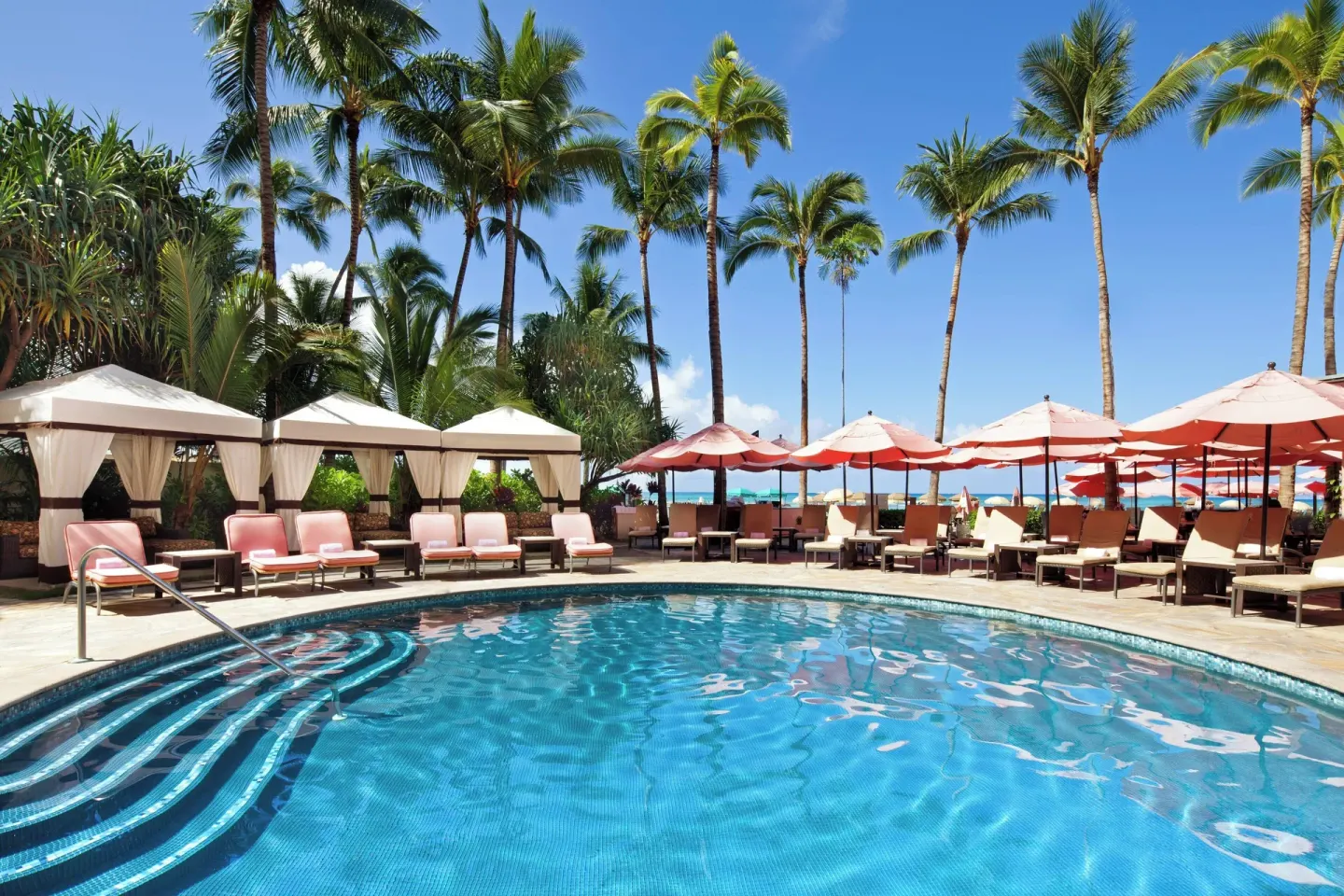 Sunny pool with cabanas, pink umbrellas and palm trees at The Royal Hawaiian, Waikiki.