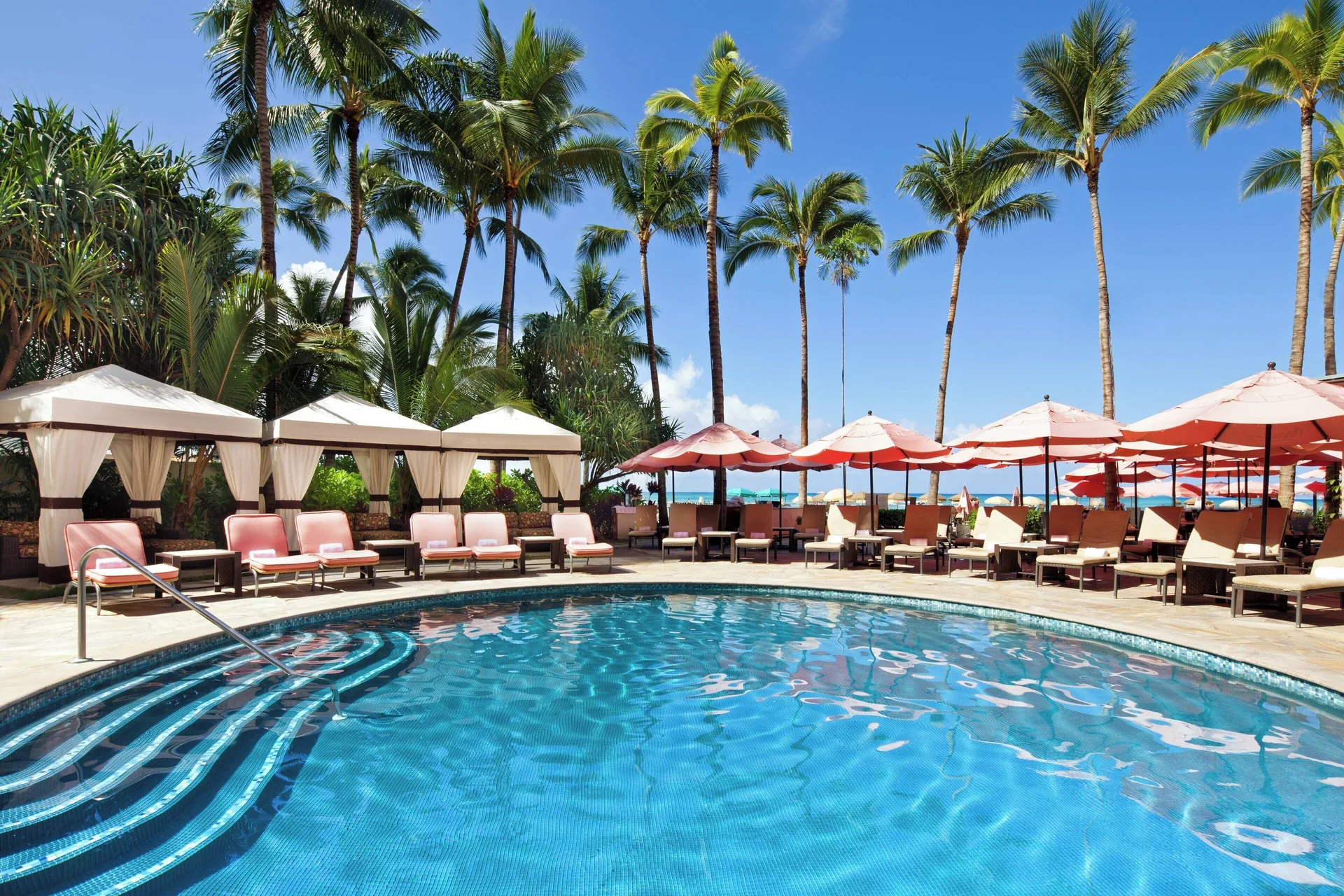 Sunny pool with cabanas, pink umbrellas and palm trees at The Royal Hawaiian, Waikiki.