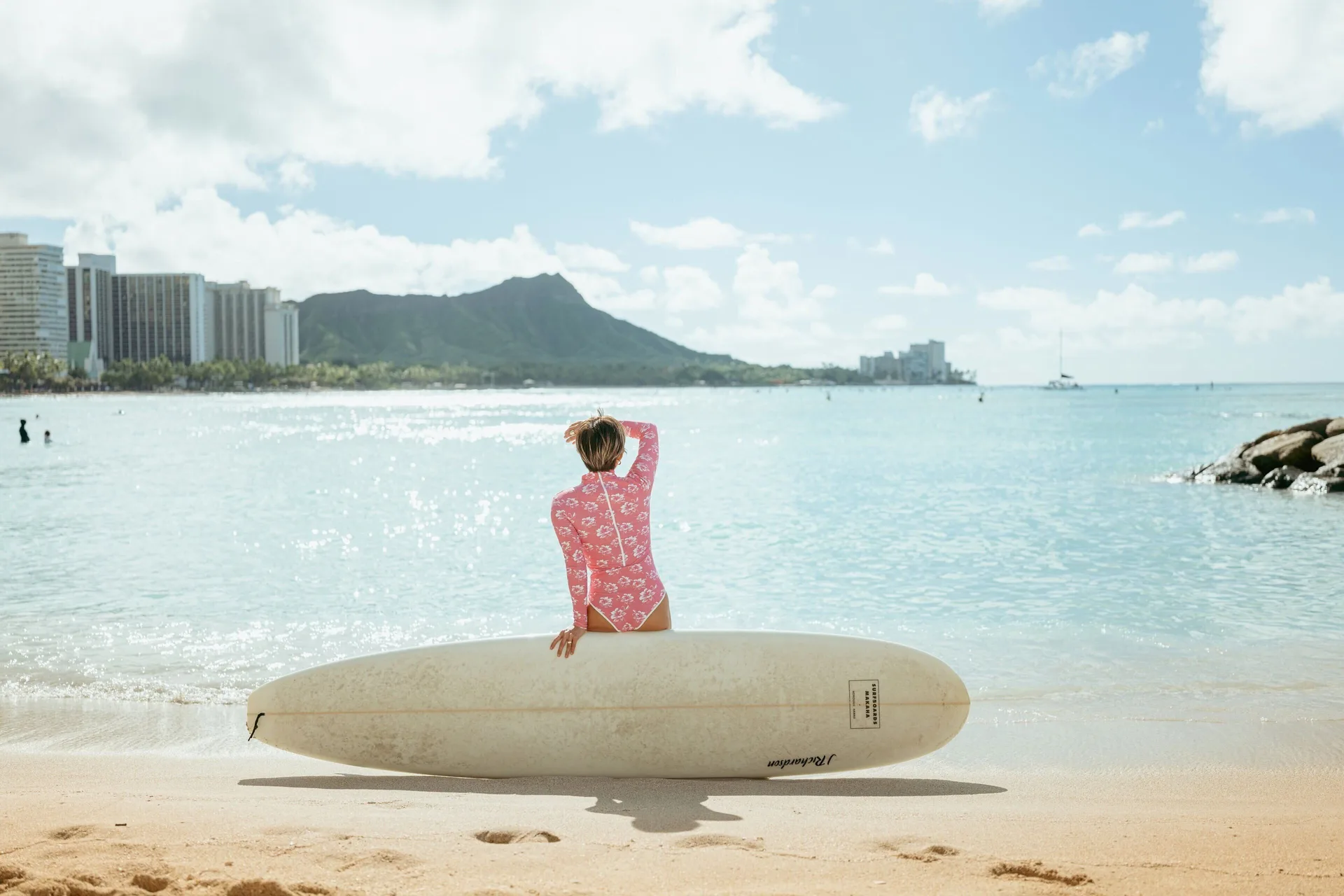 Surfer with a longboard faces Waikiki Beach and Diamond Head at The Royal Hawaiian, Waikiki.
