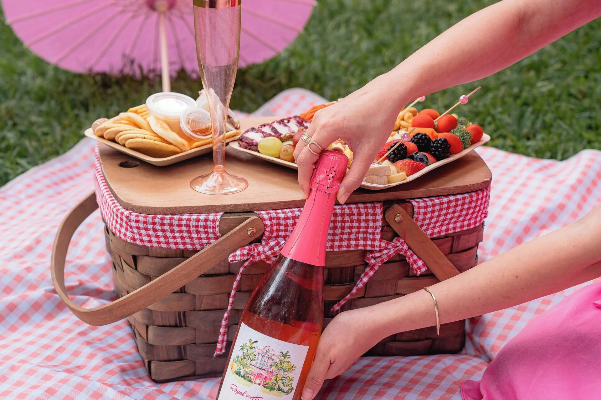 A picnic basket with fruit, crackers, and a pink drink is set on a blanket at The Royal Hawaiian, Waikiki.
