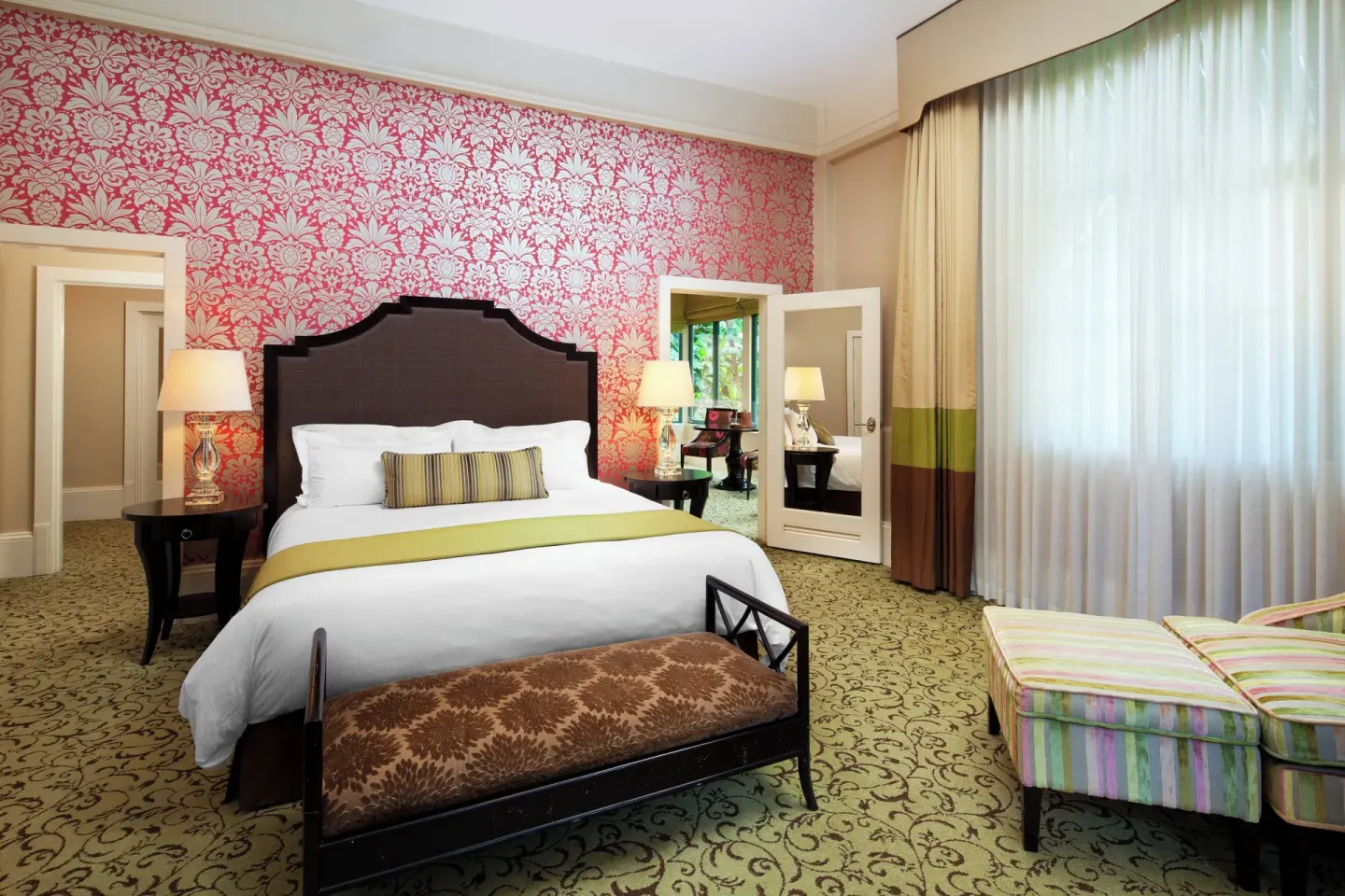 Garden View Historic Wing suite king bed at The Royal Hawaiian, Waikiki with pink floral wall and lounge chair.