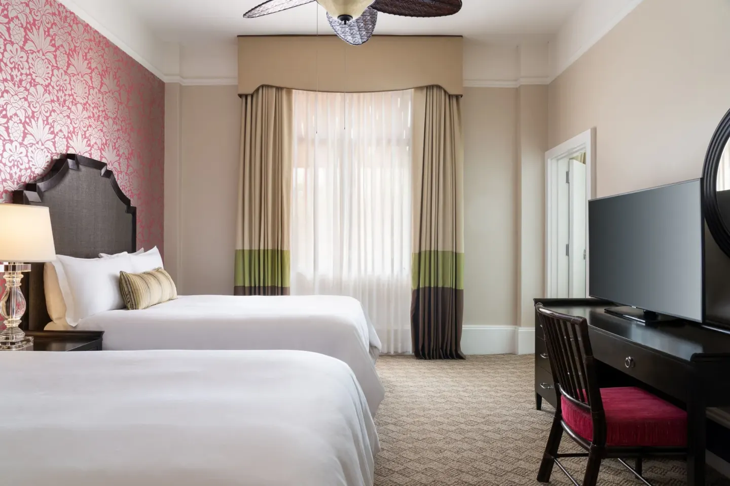 Two-bed Garden View Historic Wing room at The Royal Hawaiian, Waikiki with desk, TV and tall curtains.