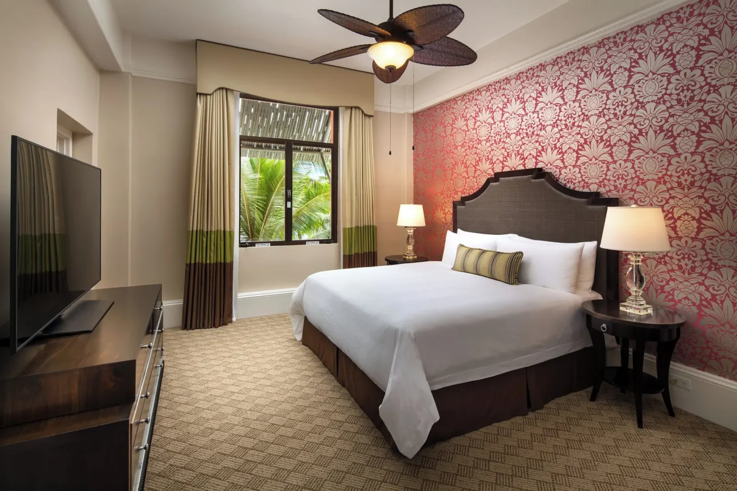 King bedroom with pink patterned wall in an ocean-view suite at The Royal Hawaiian, Waikiki.