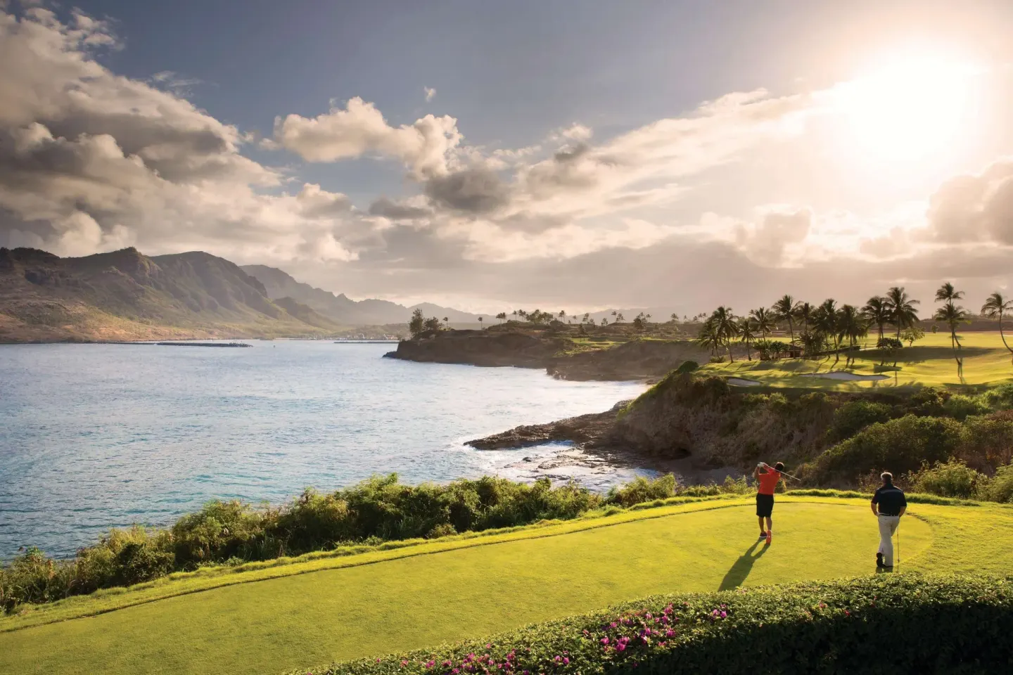 Golfers play a coastal green near The Royal Sonesta Kaua'i Resort Lihue with ocean and mountain views.