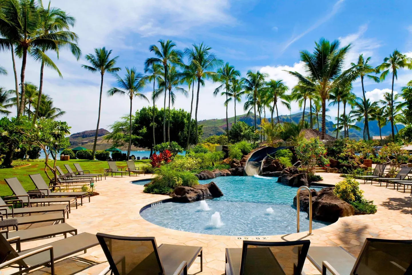 Resort pool with lounge chairs, palms and waterslide at The Royal Sonesta Kaua'i Resort Lihue.