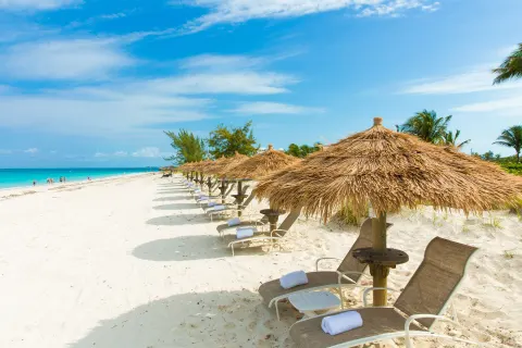 Beach loungers with thatched umbrellas along the sand at The Sands at Grace Bay.
