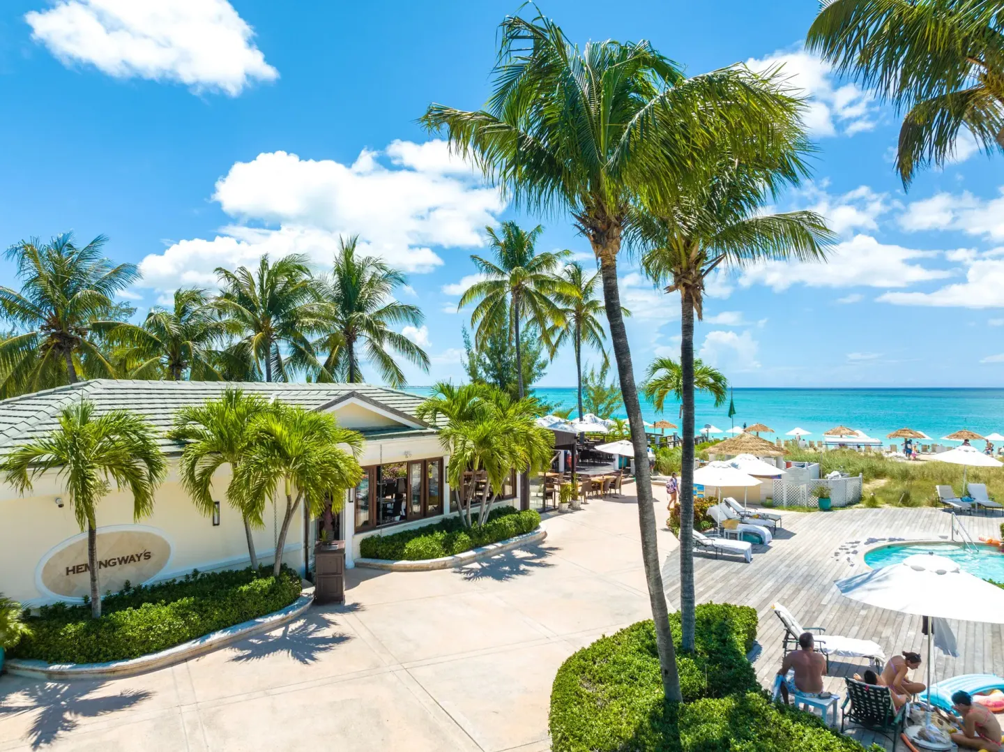 Palm trees, a beachfront building, and pool deck appear at The Sands at Grace Bay.