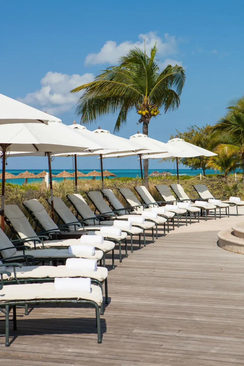 Pool deck loungers with white umbrellas and ocean beyond at The Sands at Grace Bay.