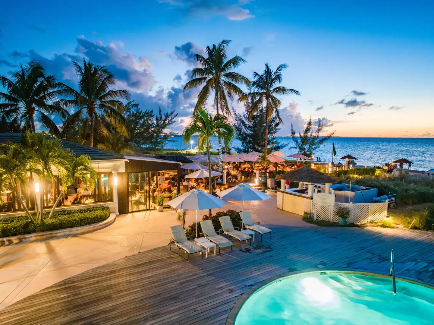 Twilight pool deck, beachfront dining area, and palms at The Sands at Grace Bay.