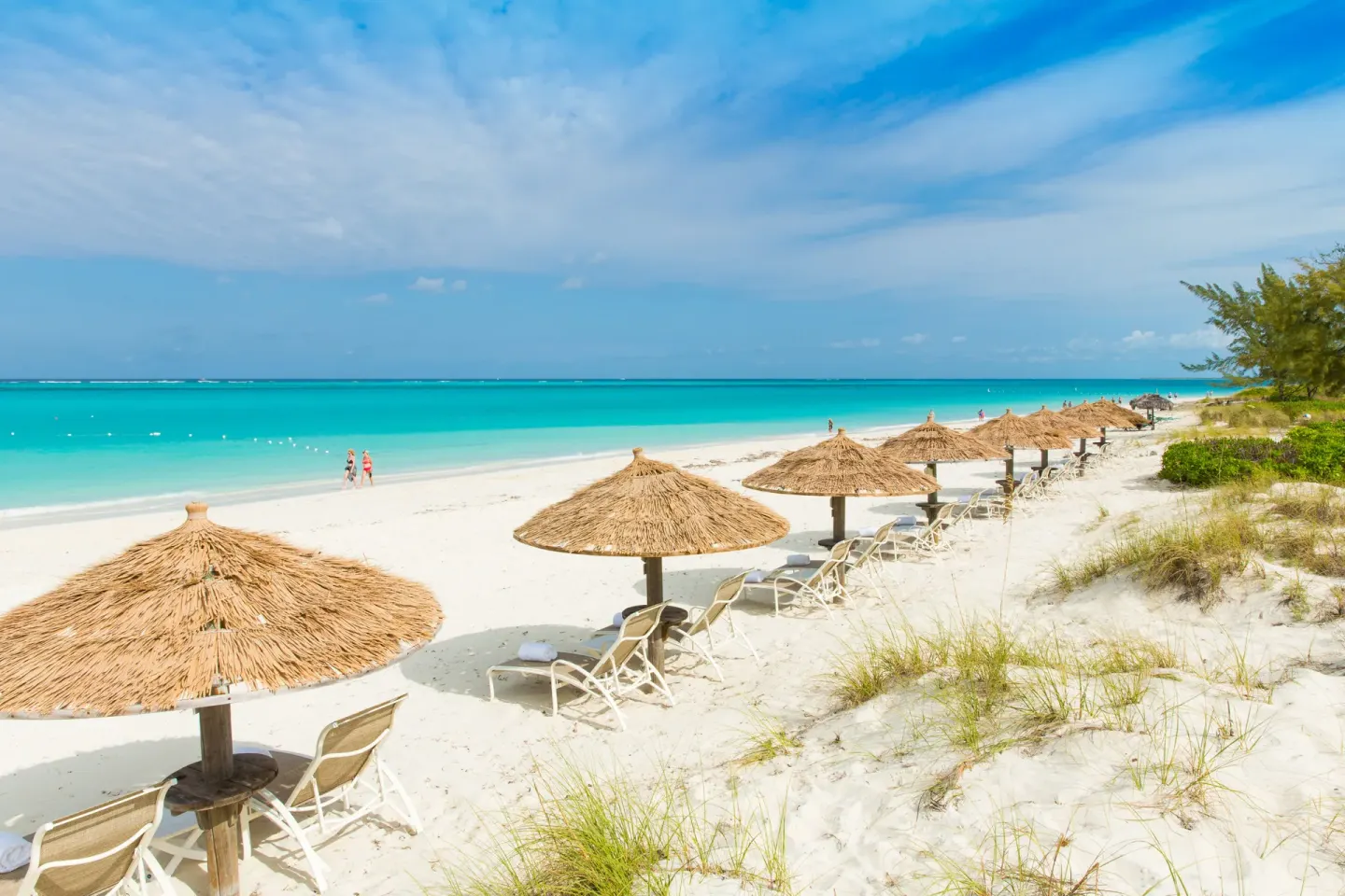 Wide beach view with thatched umbrellas and turquoise water at The Sands at Grace Bay.