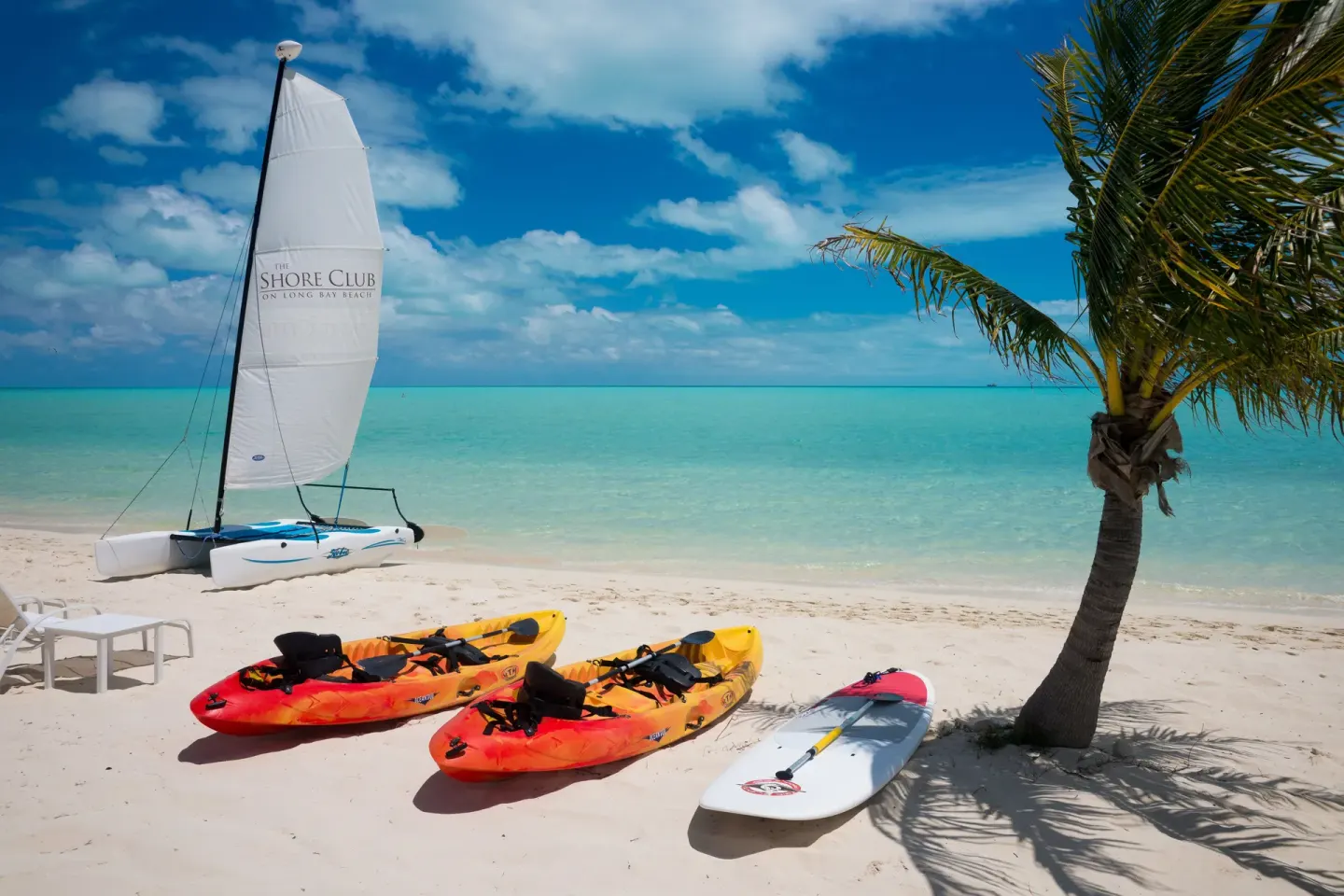 Kayaks, paddleboard, and sailboat on the beach at The Shore Club Turks and Caicos.
