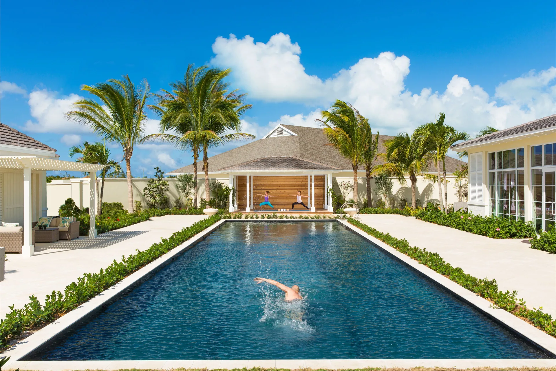 Lap pool with a swimmer, palms, and yoga deck at The Shore Club Turks and Caicos.