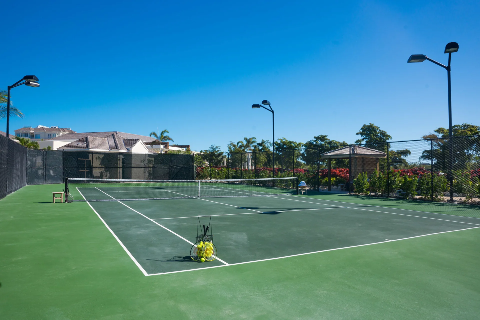 Tennis court with net, ball basket, and surrounding fencing at The Shore Club Turks and Caicos.
