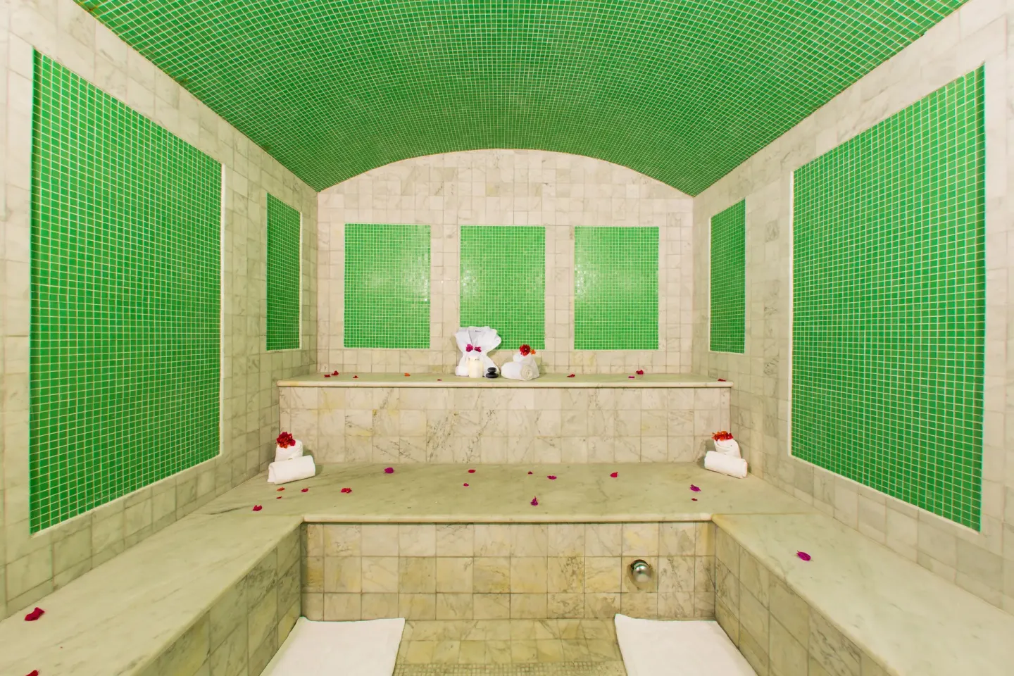 Steam room with green tile panels, marble benches, towels, and petals at The Somerset on Grace Bay.
