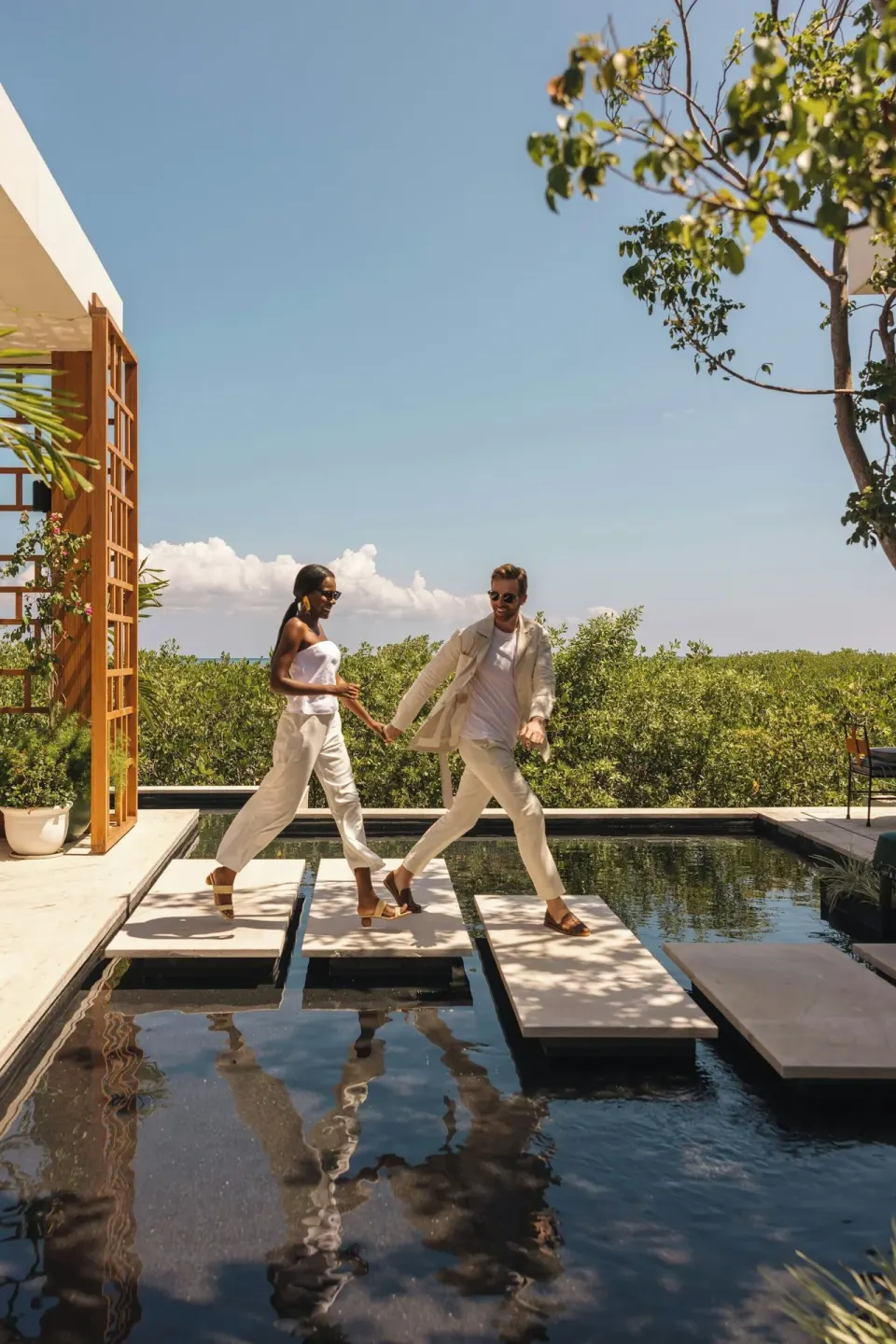 Guests crossing stepping stones over a reflecting pool at The St. Regis Kanai Resort, Riviera Maya.