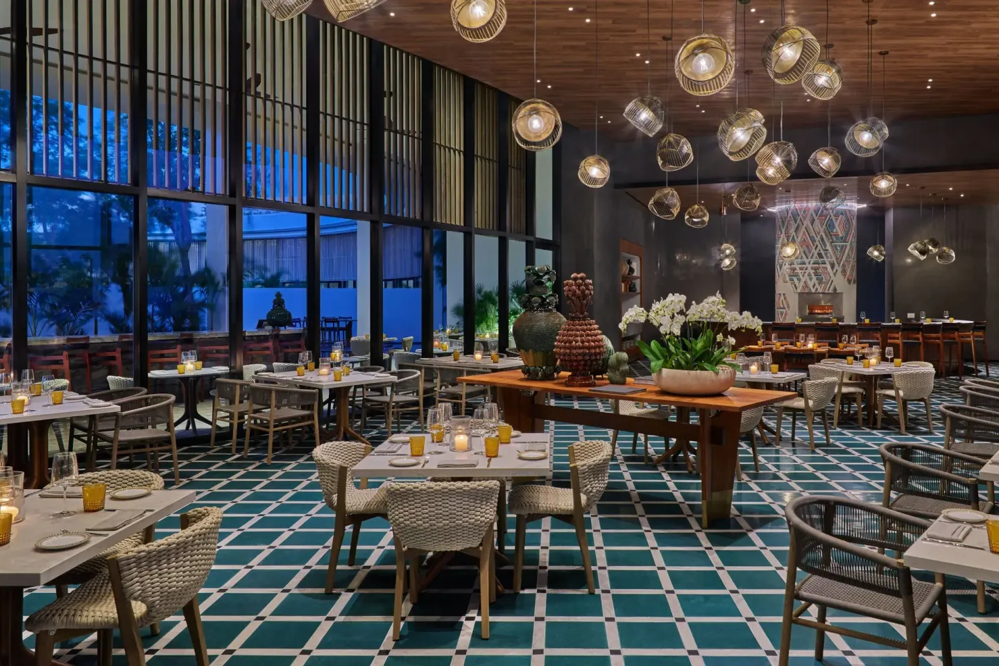 Restaurant dining room with woven chairs, pendant lights, and patterned floor at The St. Regis Kanai Resort.