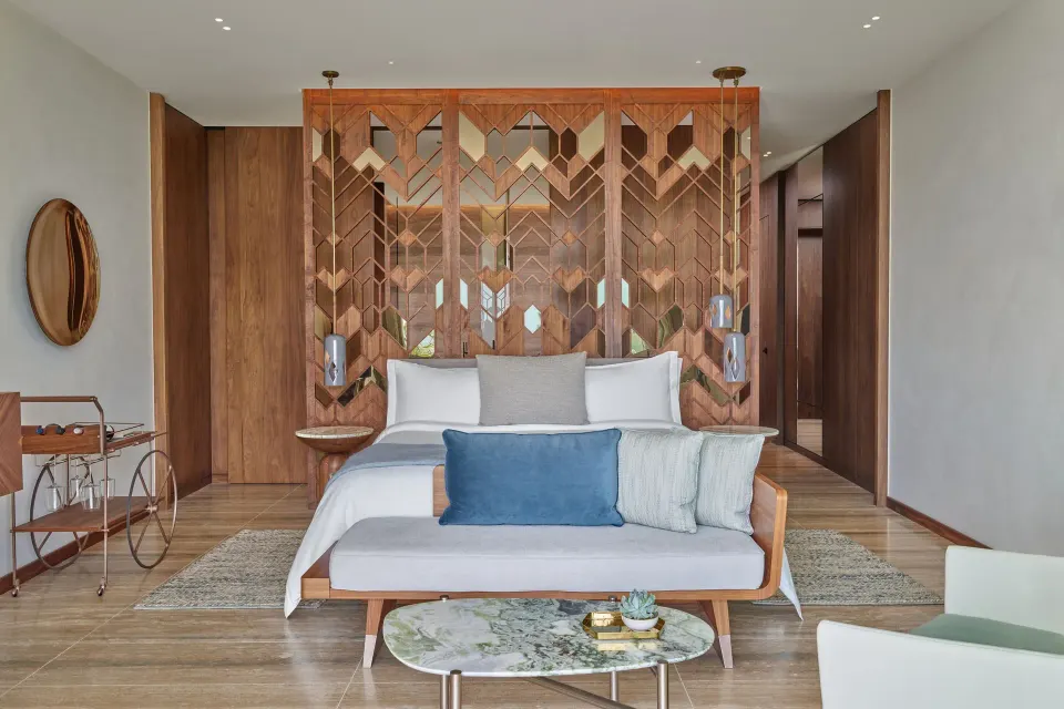 Deluxe Room king bed with sofa and patterned wood screen at The St. Regis Kanai Resort, Riviera Maya.