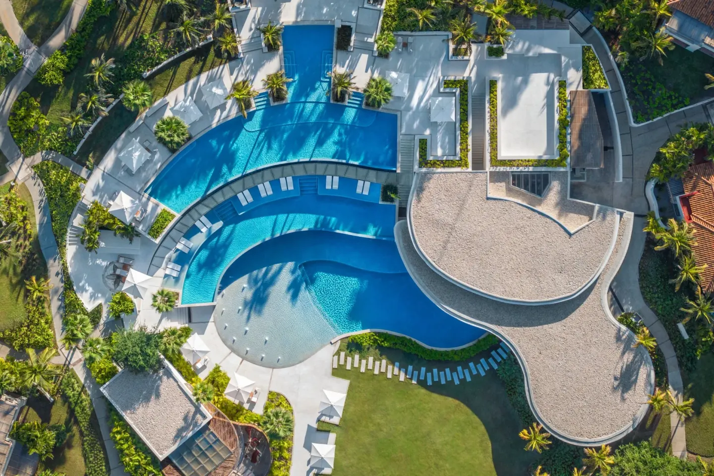 Aerial view of curved pools, sun loungers and tropical landscaping at The St. Regis Punta Mita Resort.