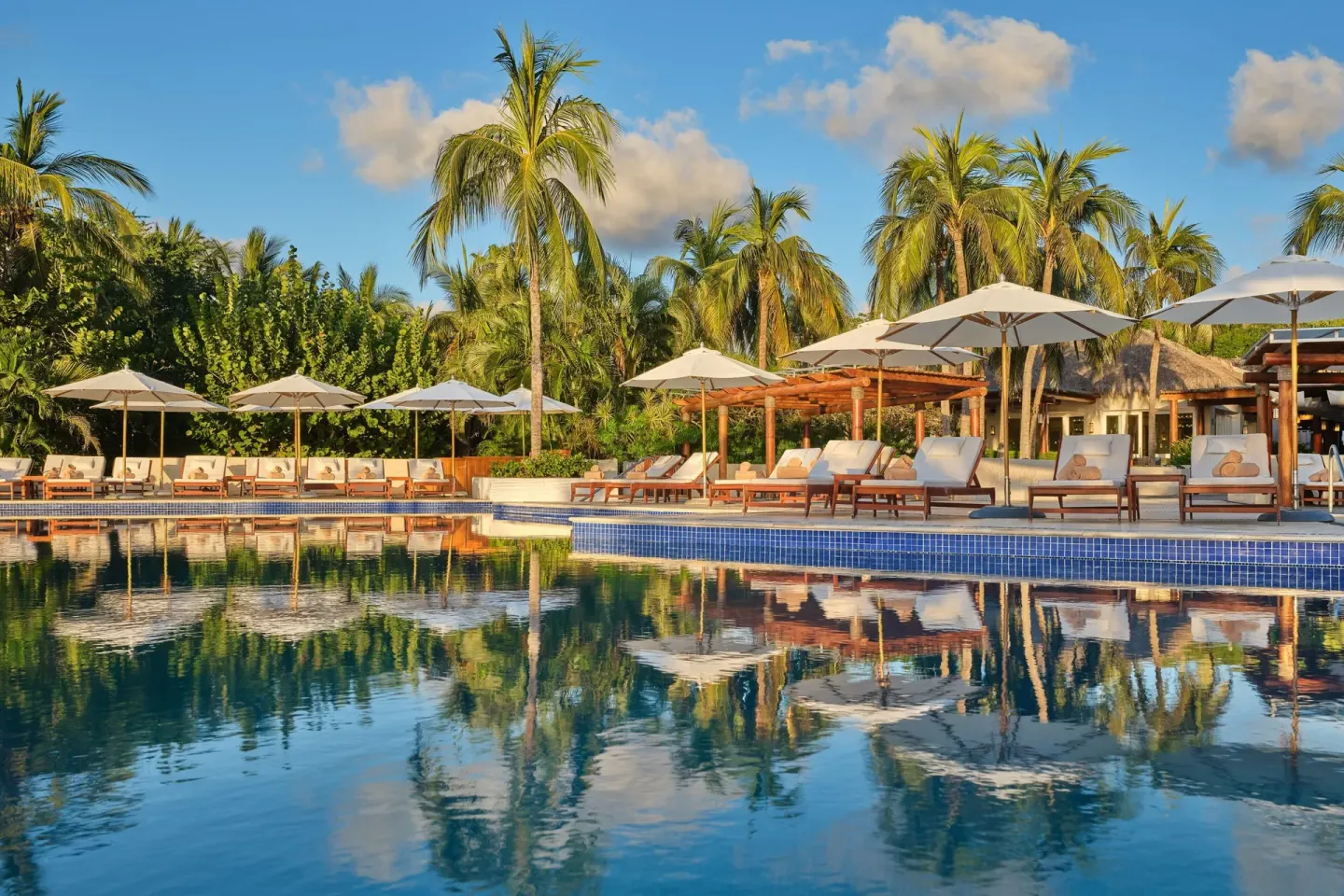 Pool deck with white umbrellas, loungers and palm reflections at The St. Regis Punta Mita Resort.
